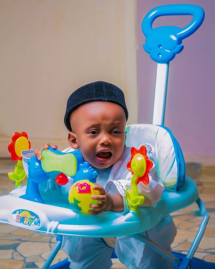 Emotional baby in walker with colorful toys inside a room.