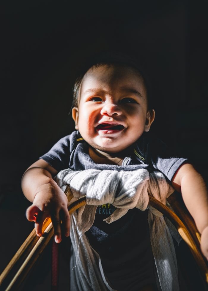 Adorable funny Asian toddler boy learning to walk in baby walker and looking at camera happily against black background